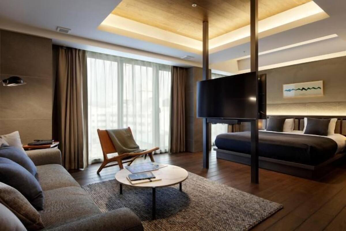 A modern hotel room with a large bed, a sofa, a television, and a desk.