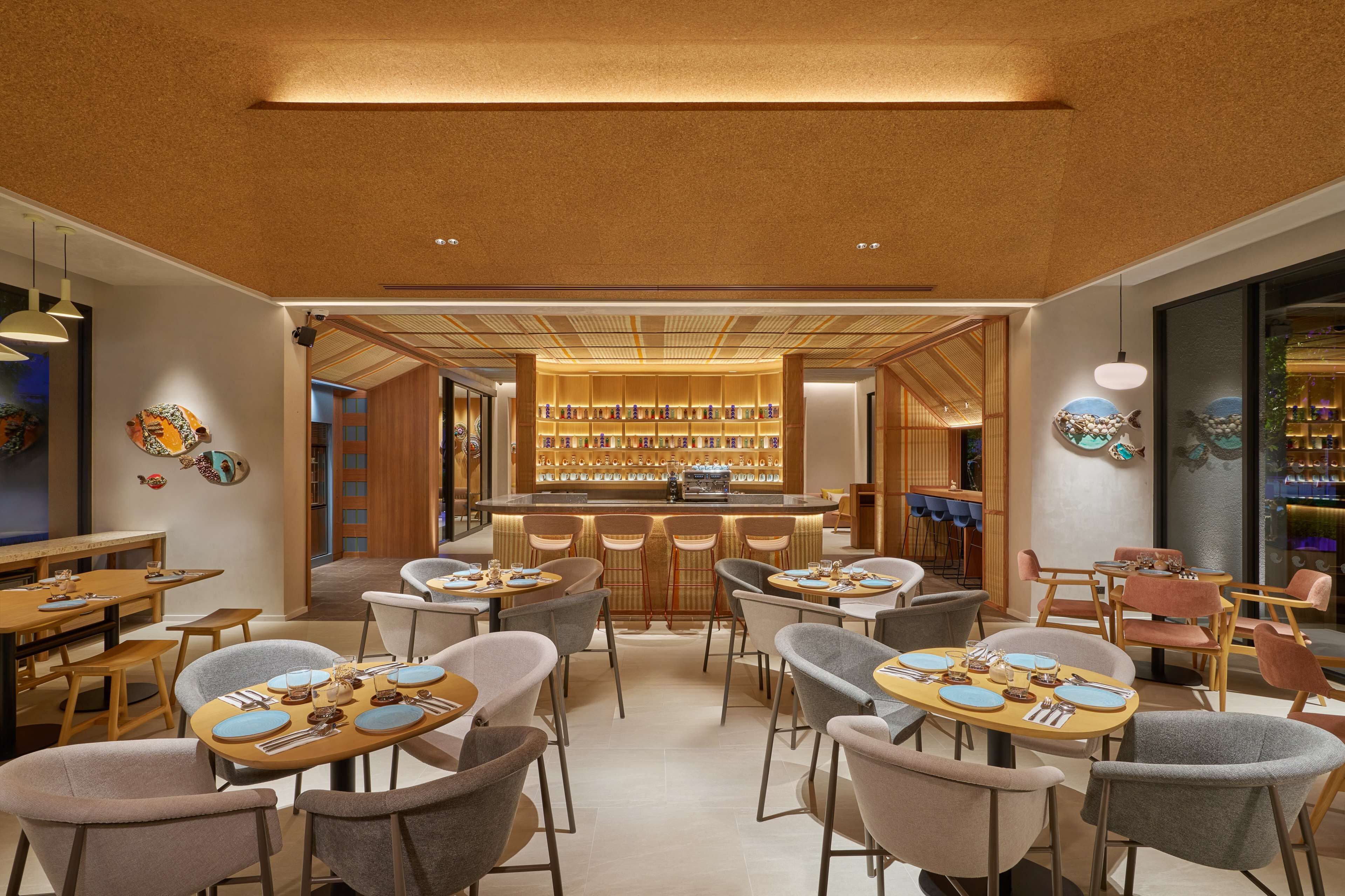 En moderne restaurant med runde borde og barsæder, med en central disk med udstilling af flasker.