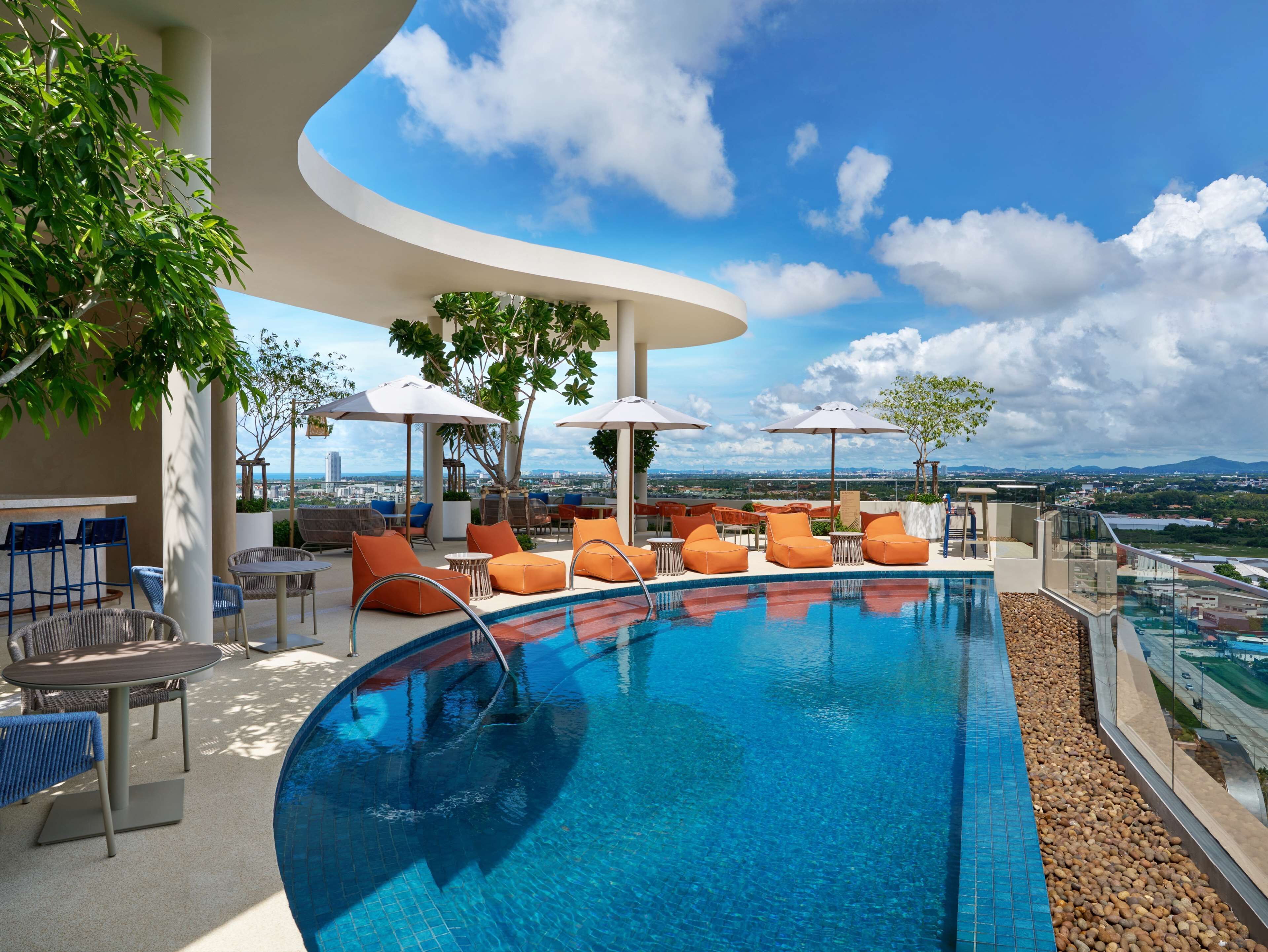 A rooftop pool area with lounge chairs and umbrellas, a clear view of the cityscape, and a pool with a pebble border. - Hilton Garden Inn Rayong (Rayong)