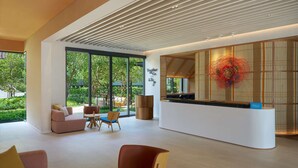 A modern hotel lobby with a reception desk, seating area, and large windows offering a view of greenery. - Hilton Garden Inn Rayong (Rayong)
