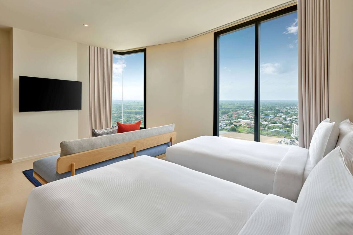Una habitación de hotel moderna con dos camas, un televisor de pantalla plana, ventanas amplias y vistas a la ciudad.