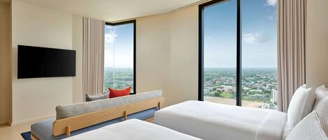 A modern hotel room with two beds, a flat-screen TV, large windows, and a city view.