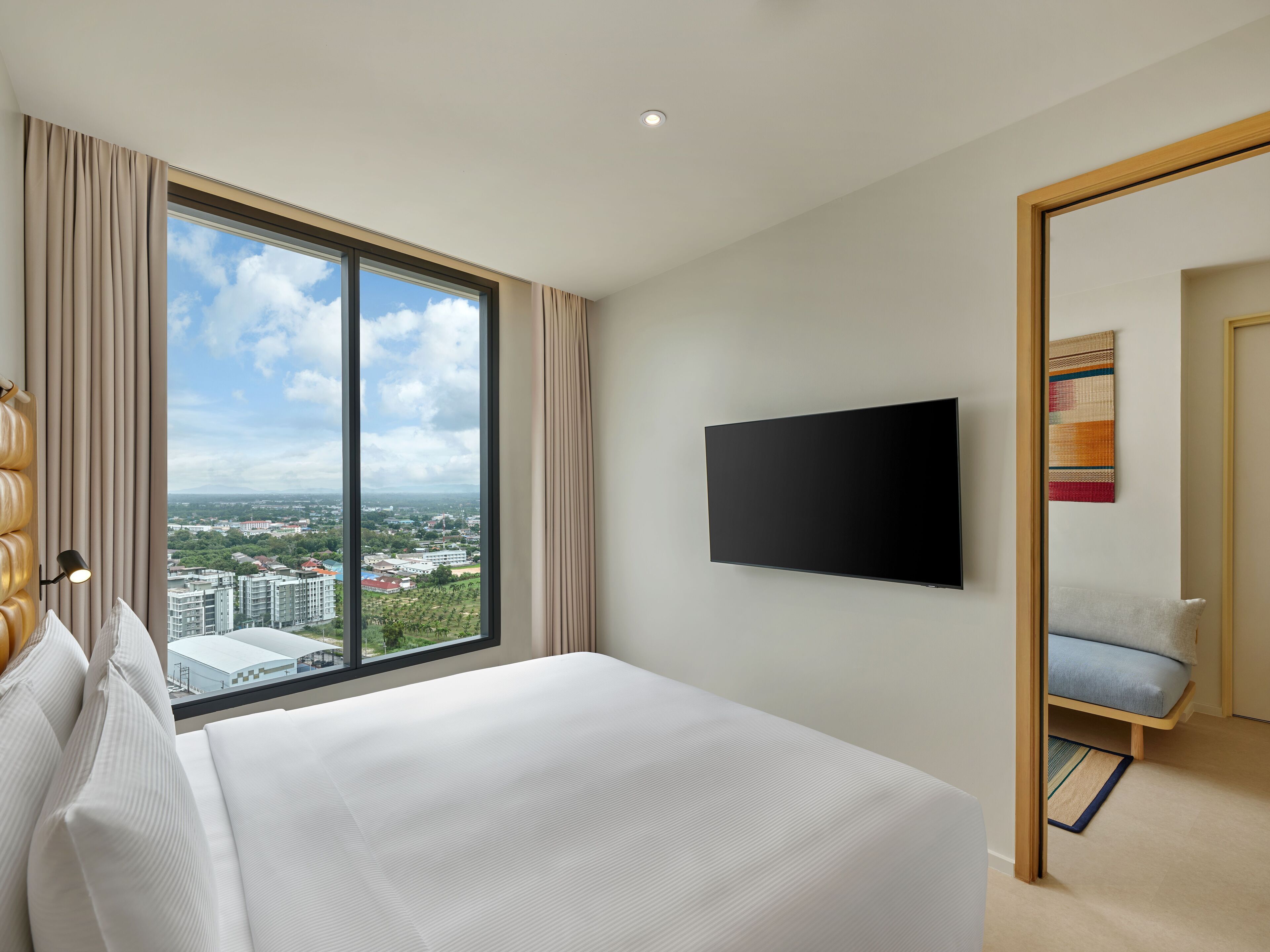 Habitación de hotel con un ventanal grande, una cama, un televisor de pantalla plana y una pequeña zona de estar.