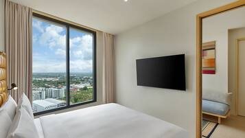 Habitación de hotel con un ventanal grande, una cama, un televisor de pantalla plana y una pequeña zona de estar.