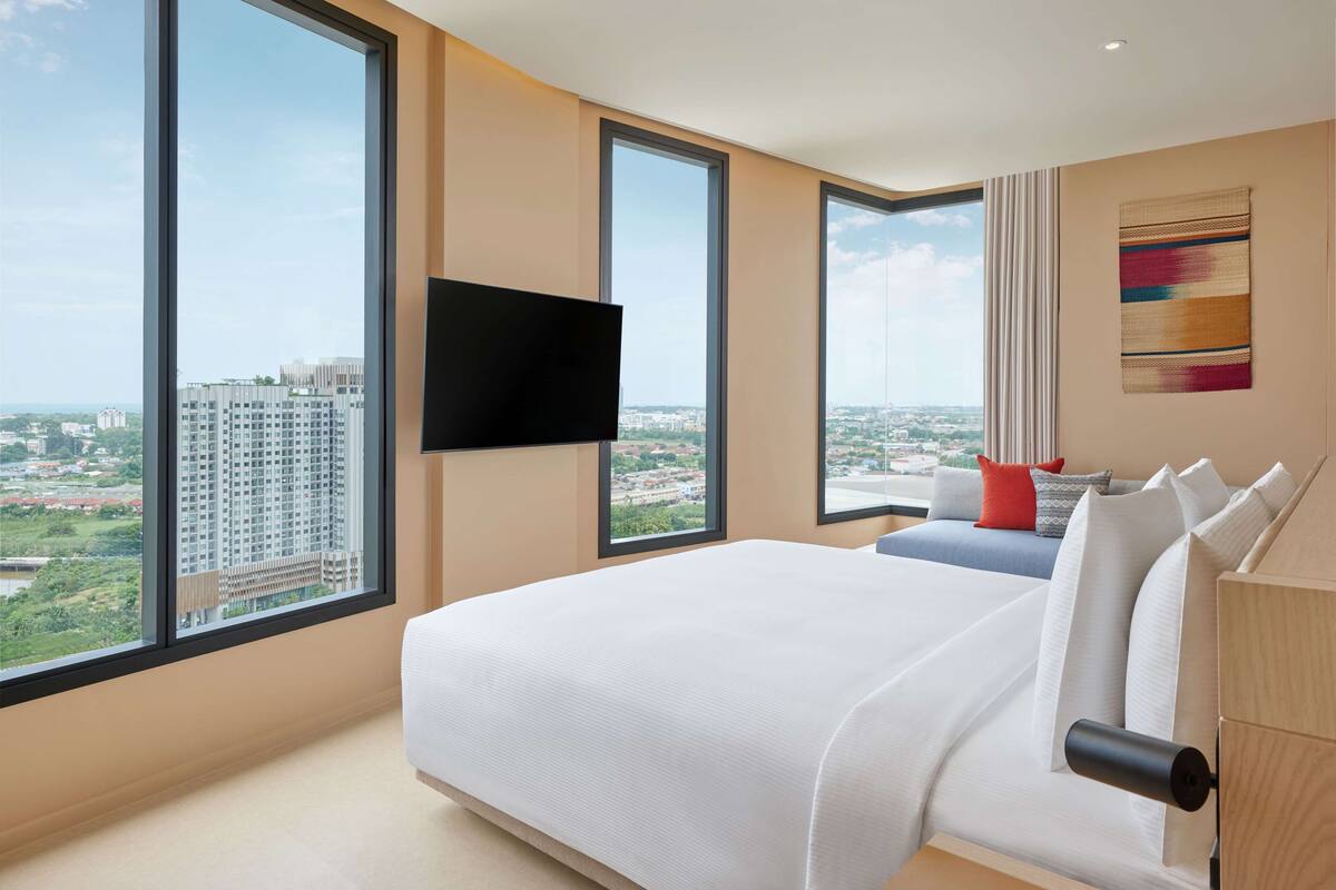Una habitación de hotel moderna con una cama grande, un televisor de pantalla plana en la pared y vistas a la ciudad a través de amplios ventanales.
