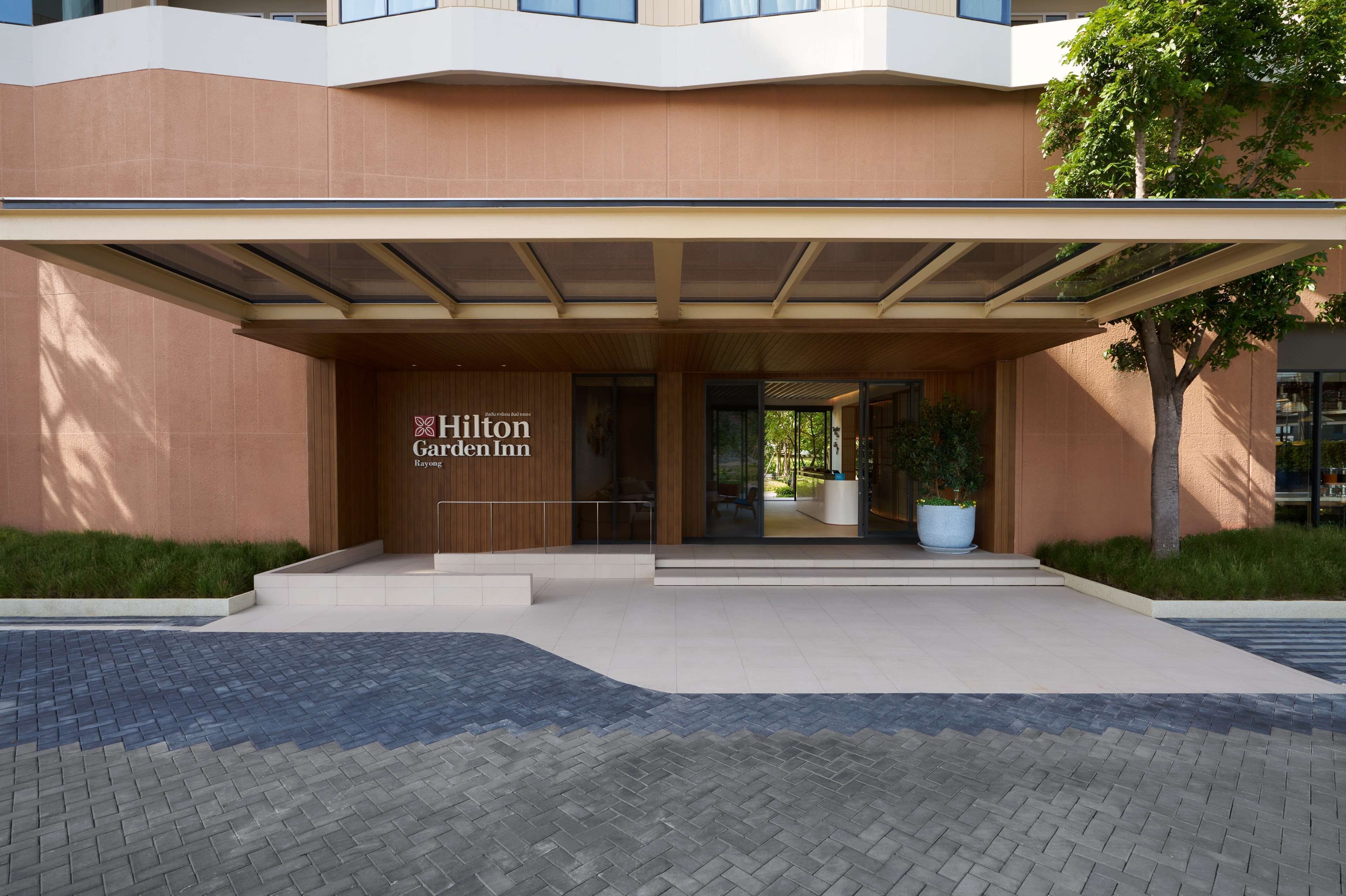 The entrance of the Hilton Garden Inn with a modern design, featuring a covered entrance, a reception desk, and a landscaped area with a large planter.