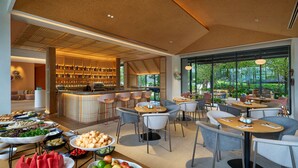 A modern dining area with a bar, seating, and a variety of food displays. - Hilton Garden Inn Rayong (Rayong)
