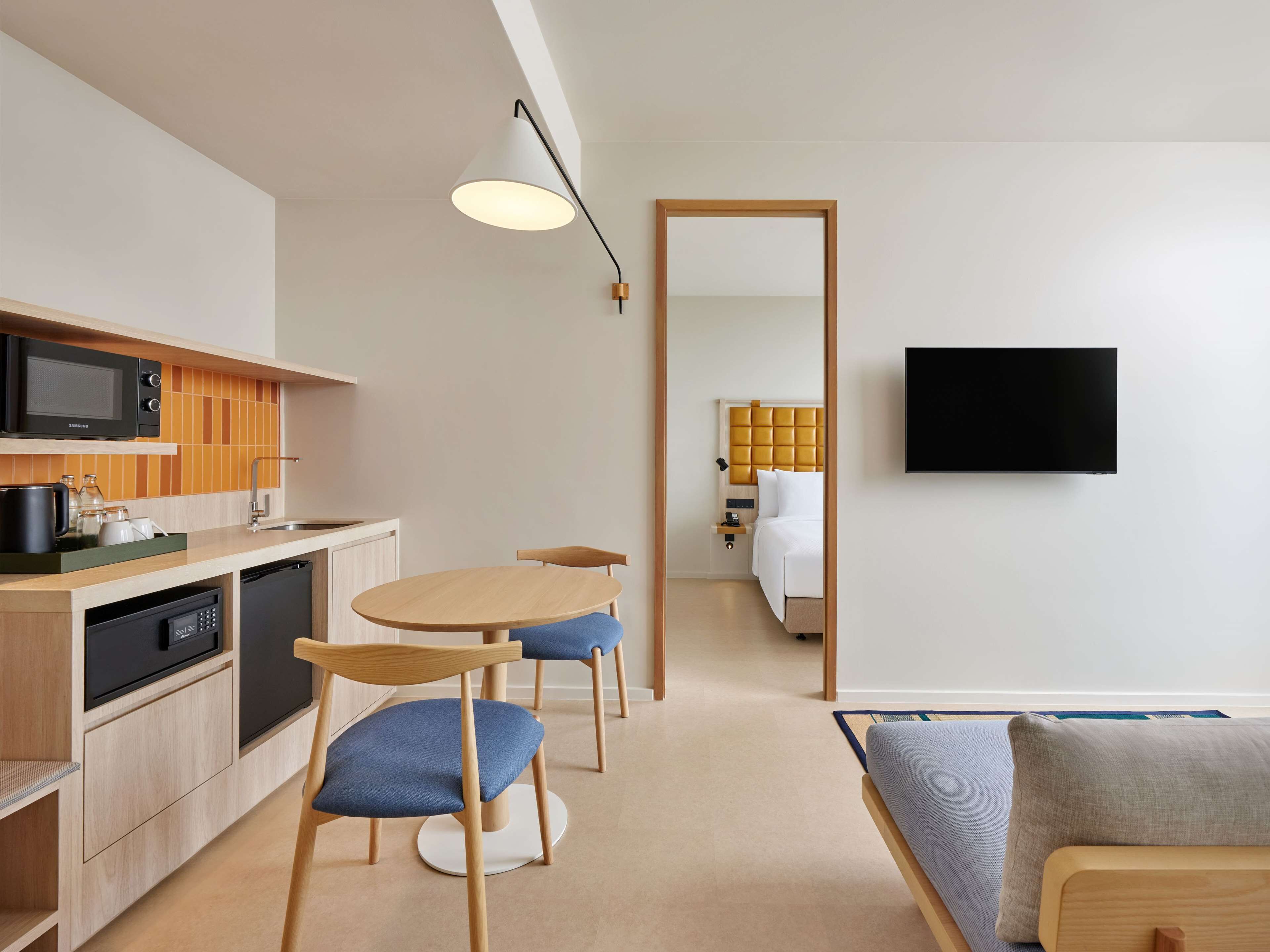 A modern hotel room with a kitchen, dining area, and a bed.