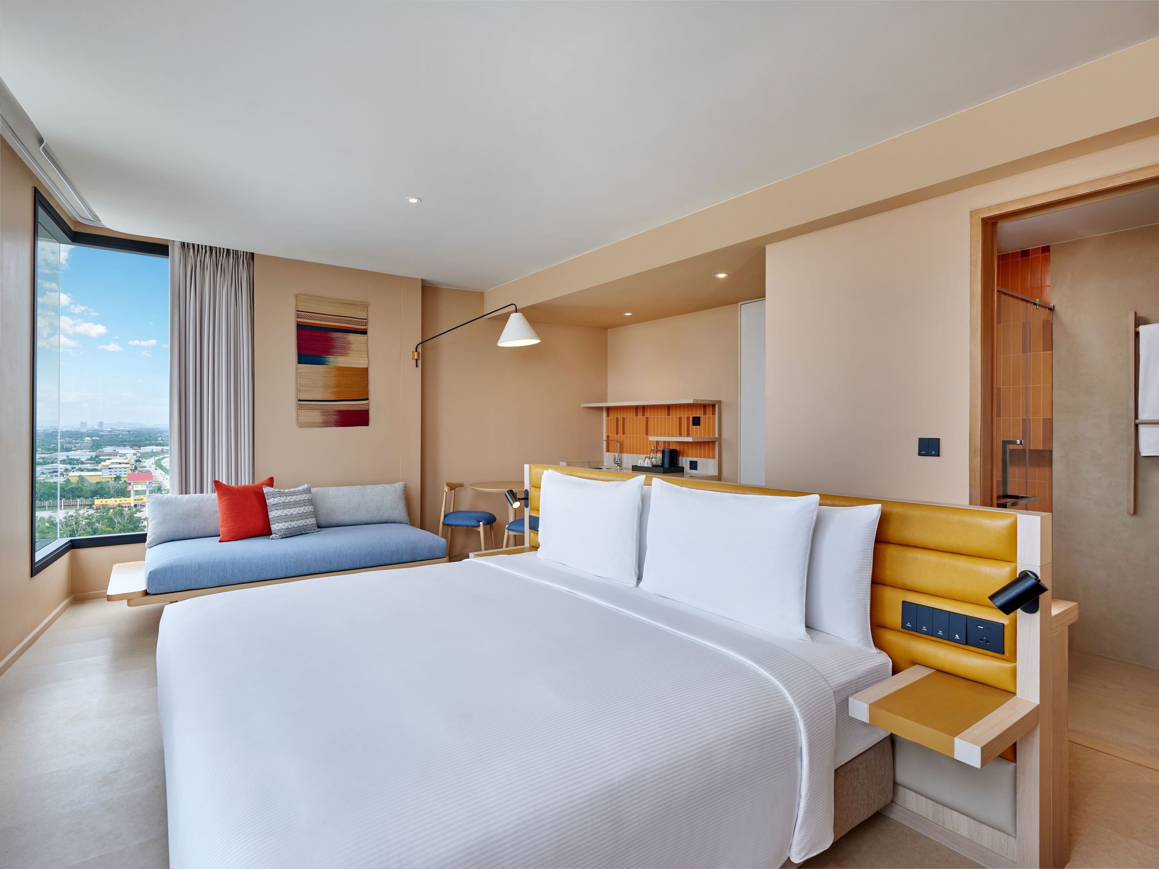 A modern hotel room with a large bed, a sofa, a small table, and a view of the city.