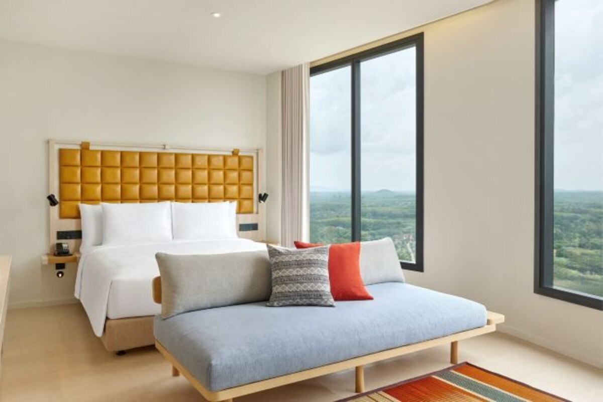 A modern hotel room with a large bed, a sofa, and a view of the countryside.
