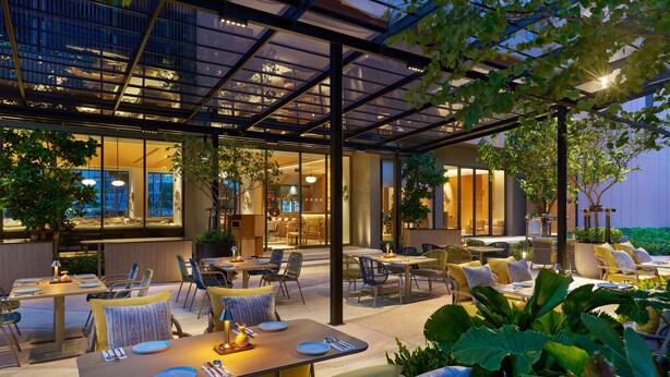 An outdoor dining area with tables and chairs, surrounded by greenery and a glass enclosure. - Hilton Garden Inn Rayong (Rayong)