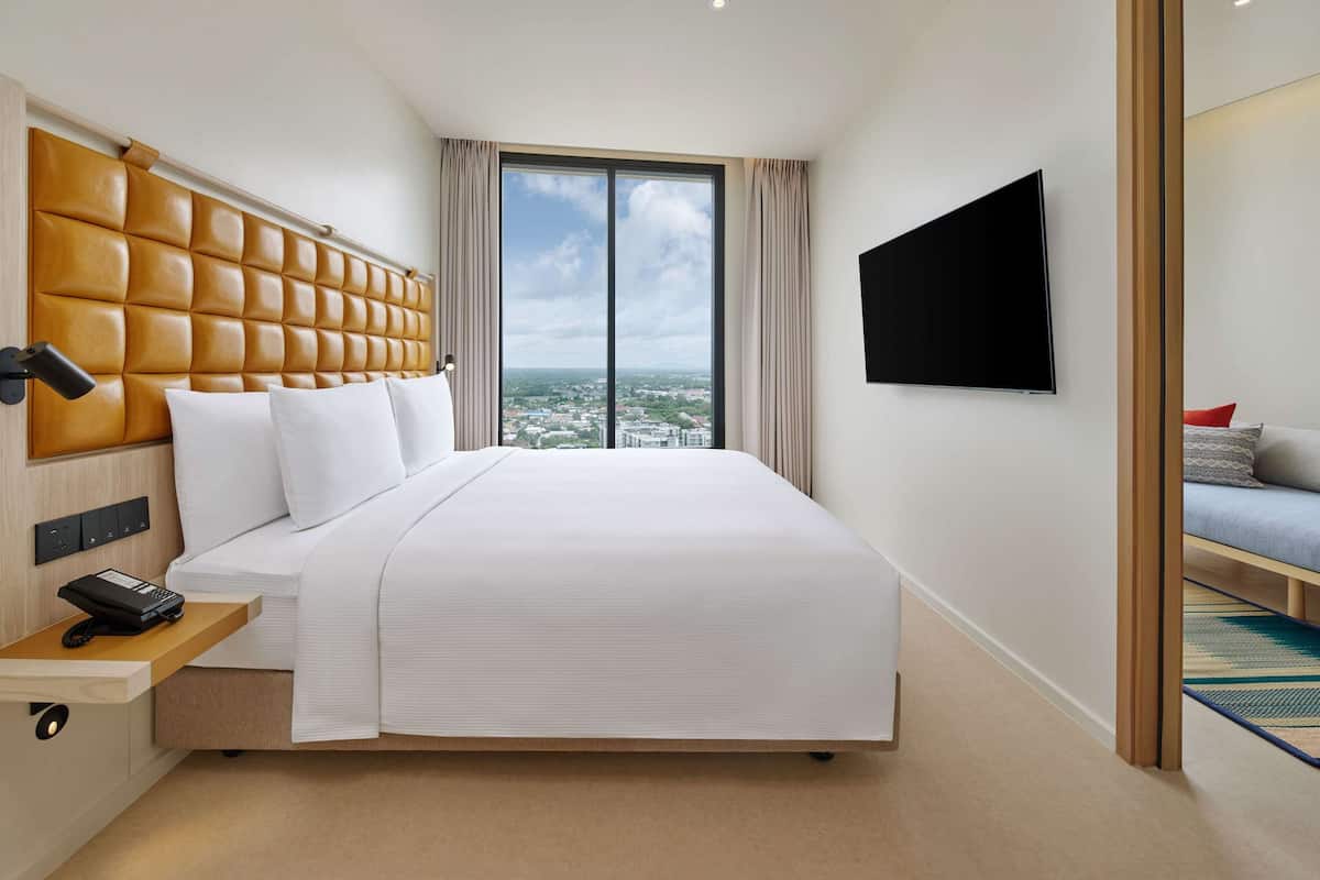 Habitación de hotel moderna con una cama grande, televisor montado y vistas a la ciudad a través de la ventana.