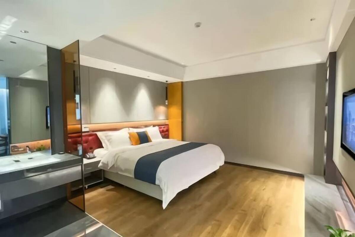 Una habitación de hotel moderna con una cama grande, una mesita de noche, un espejo y un televisor.