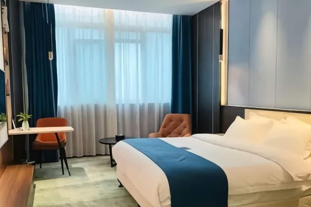 Habitación de hotel con cama, escritorio, silla, mesita y ventana con cortinas.