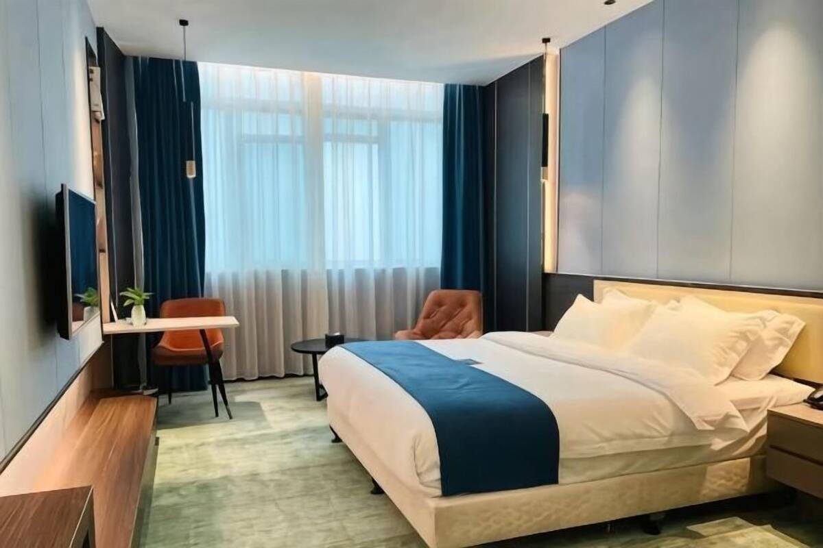 Una habitación de hotel con cama, escritorio, silla, televisor y ventana con cortinas.