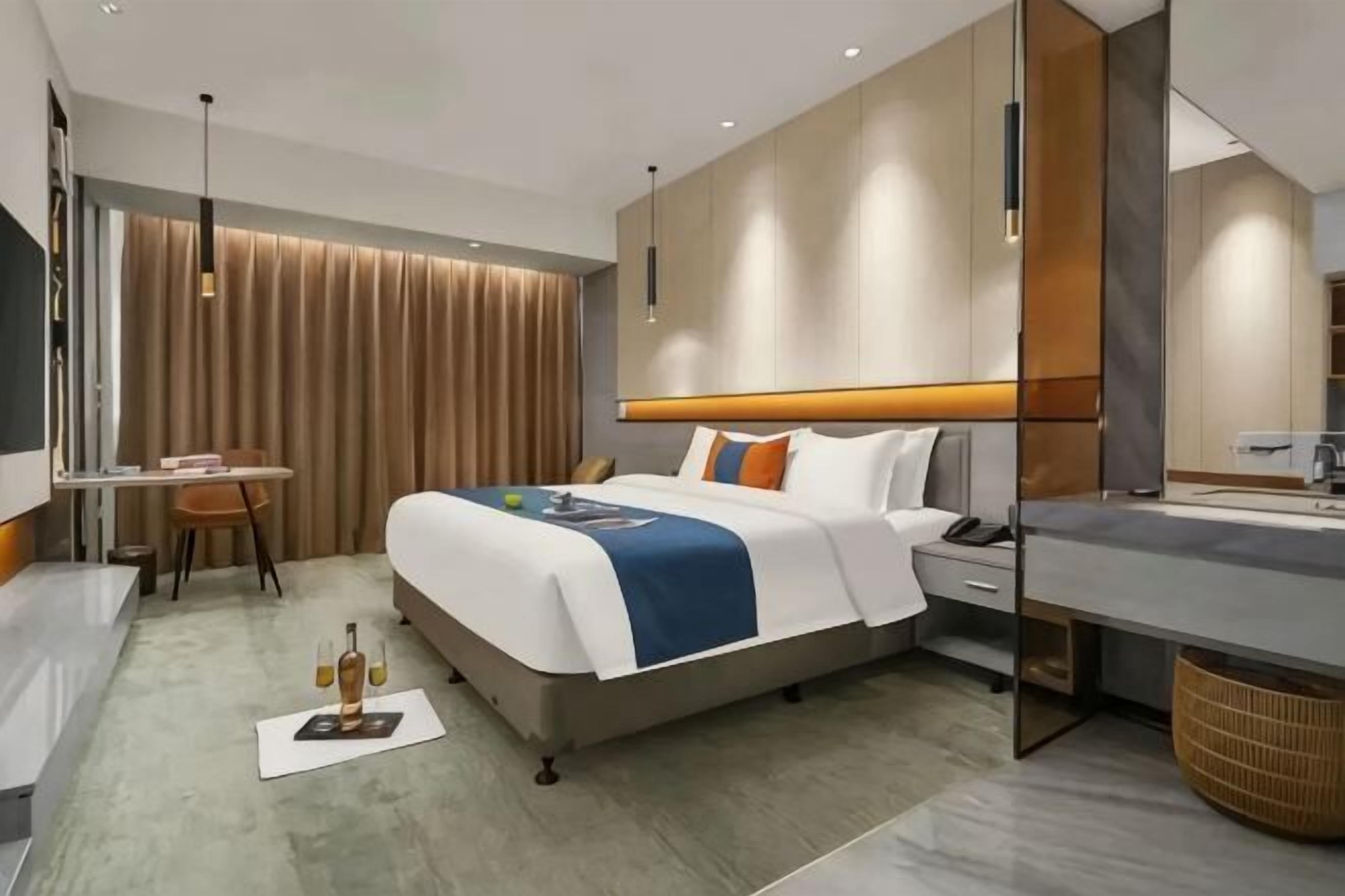 A modern hotel room with a bed, bedside table, desk, and a large mirror.