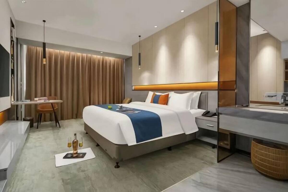 Una habitación de hotel moderna con cama, mesita de noche, escritorio y un espejo grande.