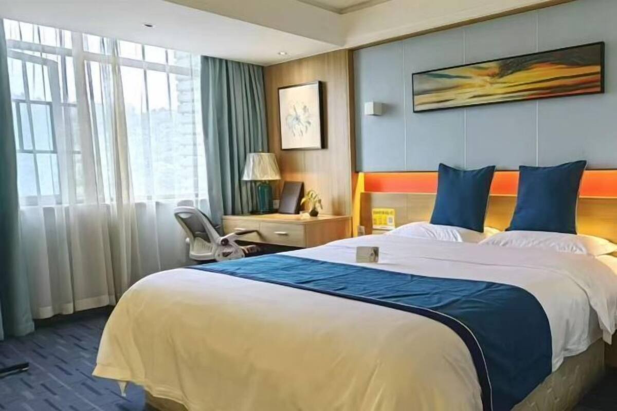 Habitación de hotel con cama, escritorio, silla, lámpara y un cuadro en la pared.