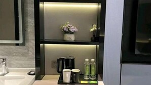 Ein modernes Badezimmer mit einem Waschbecken, einer schwarzen Ablage mit zwei Tassen, einem Wasserkocher und zwei Wasserflaschen.