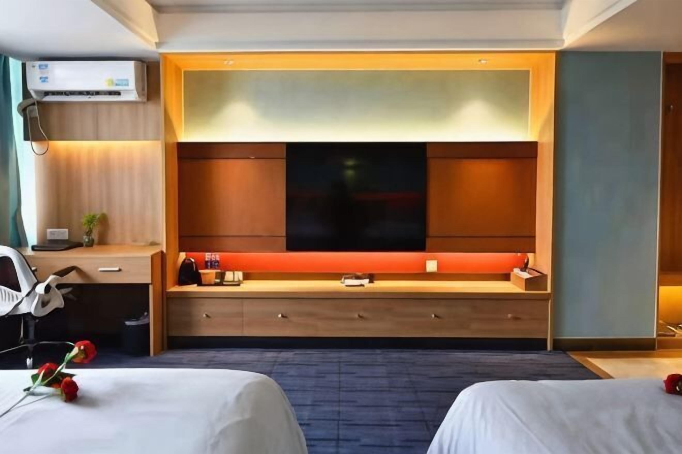 A hotel room with two beds, a TV, a desk with a chair, and a large window.