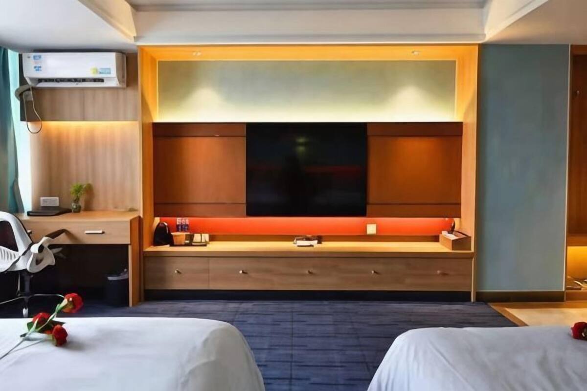 Habitación de hotel con dos camas, televisor, escritorio con silla y un ventanal grande.