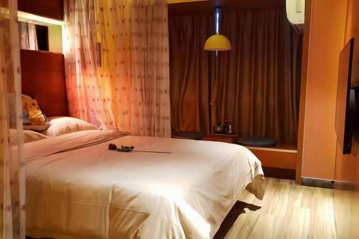 Una habitación de hotel con una cama, cortinas, una lámpara y una mesita.