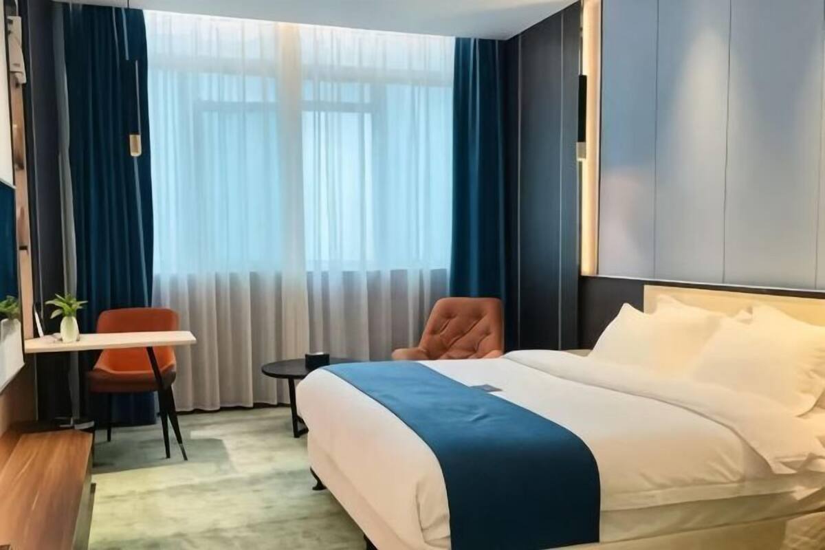 Una habitación de hotel con cama, escritorio, silla, una mesita y ventana con cortinas.