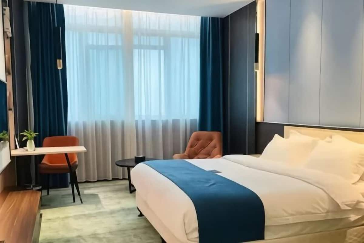 A hotel room with a bed, a desk, a chair, a small table, and a window with curtains.