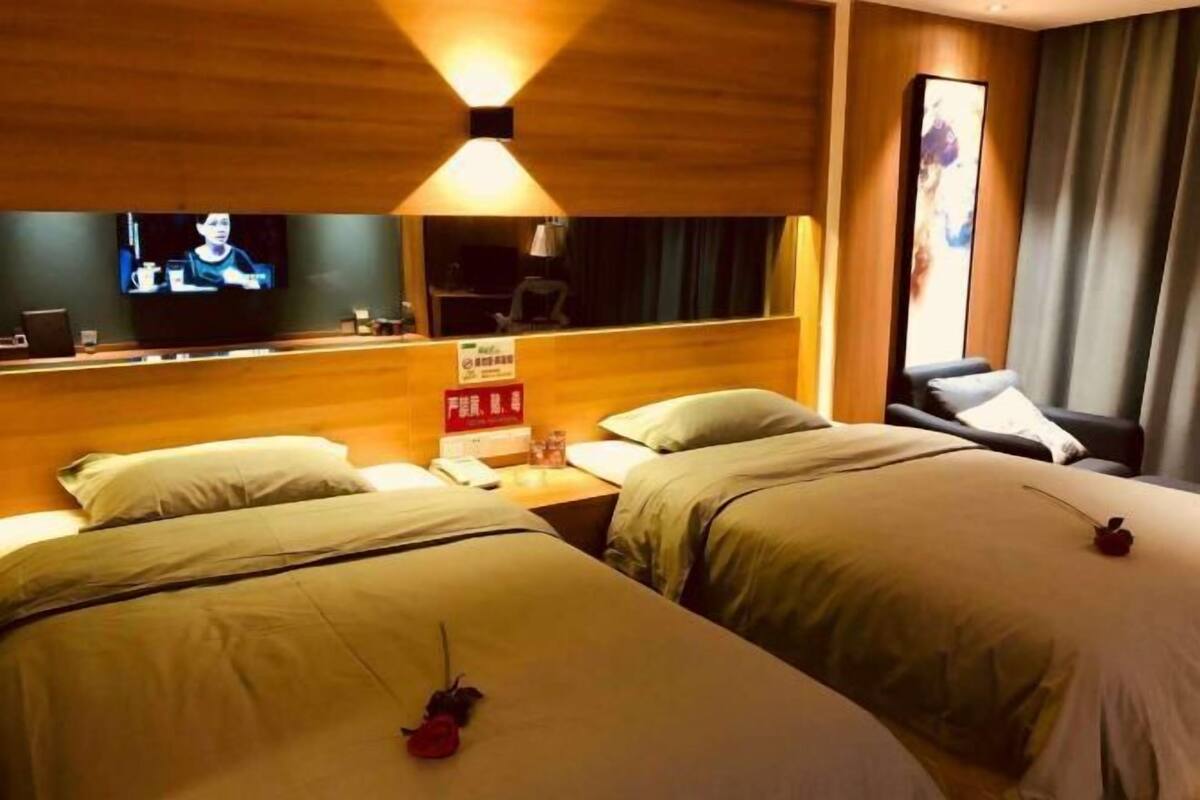 Habitación de hotel con dos camas, un televisor en la pared, un escritorio con una silla y una ventana con cortinas.
