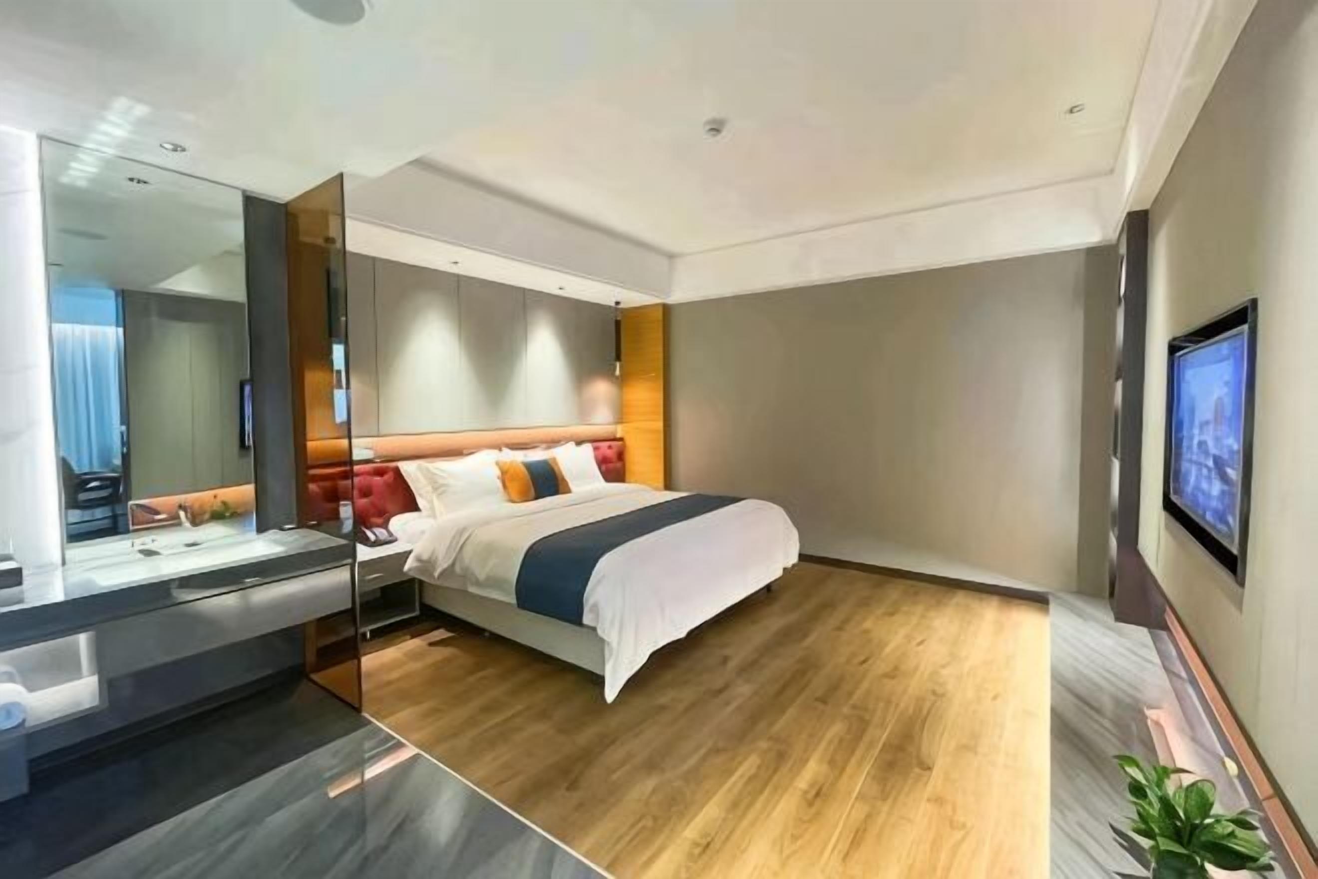 A modern hotel room with a large bed, a bedside table, a mirror, and a TV mounted on the wall.