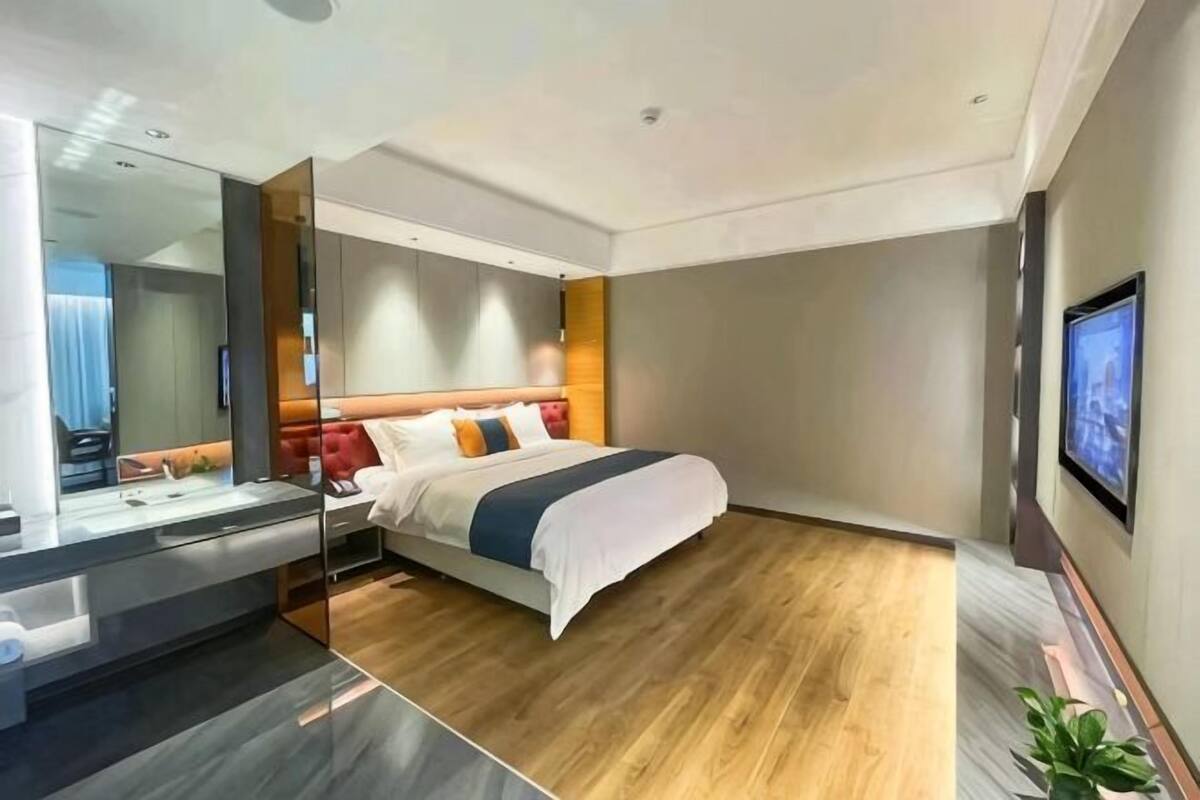 Una habitación de hotel moderna con una cama grande, una mesita de noche, un espejo y un televisor instalado en la pared.
