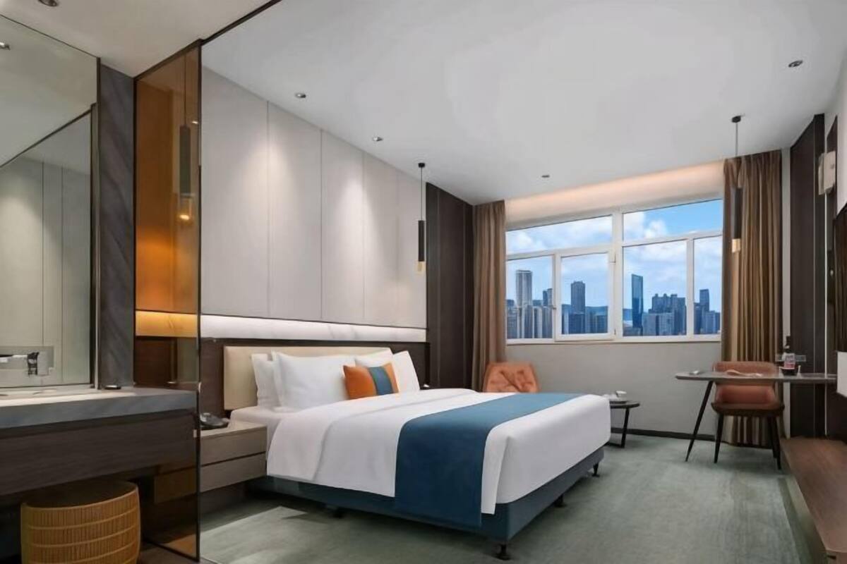 Habitación de hotel con cama, escritorio, silla, ventana y vista panorámica de la ciudad, además de un baño.