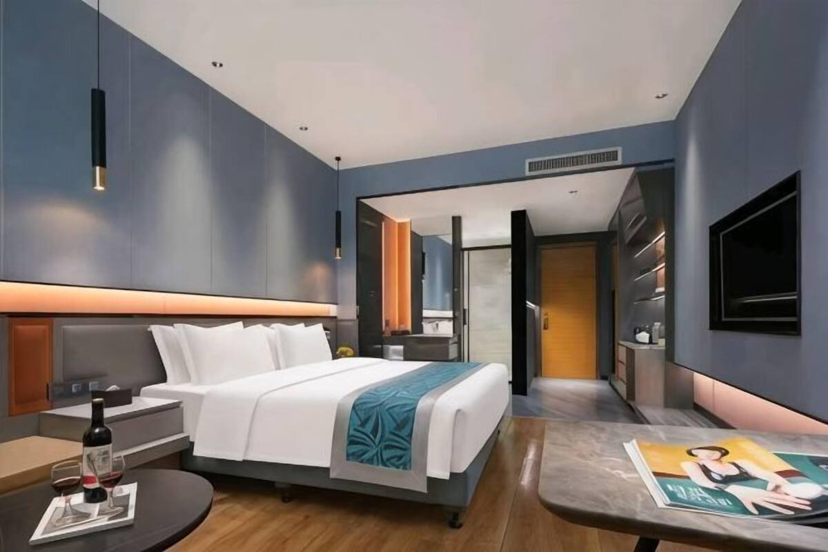 Una habitación de hotel moderna con una cama, mesita de noche, televisión y vistas a un pasillo.