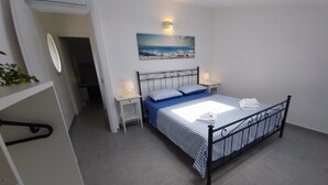 Una camera da letto ordinata con un letto, comodini, una lampada a parete e un quadro raffigurante una spiaggia.