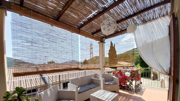 Un'area salotto all'aperto coperta, con mobili in vimini, un soffitto decorativo e vista sul paesaggio circostante.