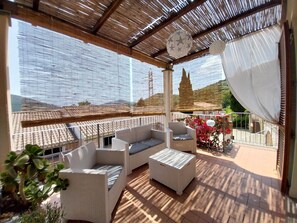 Un espace extérieur aménagé, abrité et doté de mobilier en osier, d’un plafond décoratif et d’une vue sur le paysage environnant.