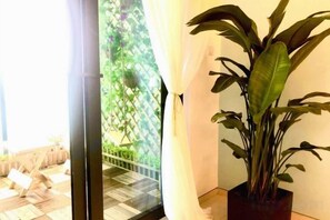 Een kamer met een potplant, een schuifdeur naar een balkon en uitzicht op groen.