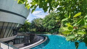A swimming pool with a curved design, surrounded by lush greenery and a modern building structure.
