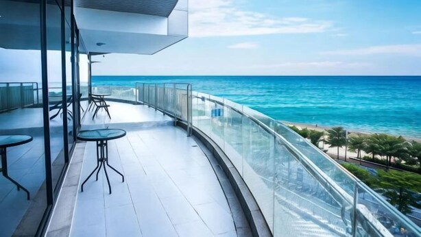 A balcony with a glass railing, a view of the ocean, and a few tables and chairs.
