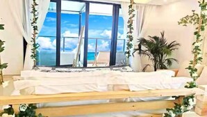 A bedroom with a bed, a view of the sky, and a plant.