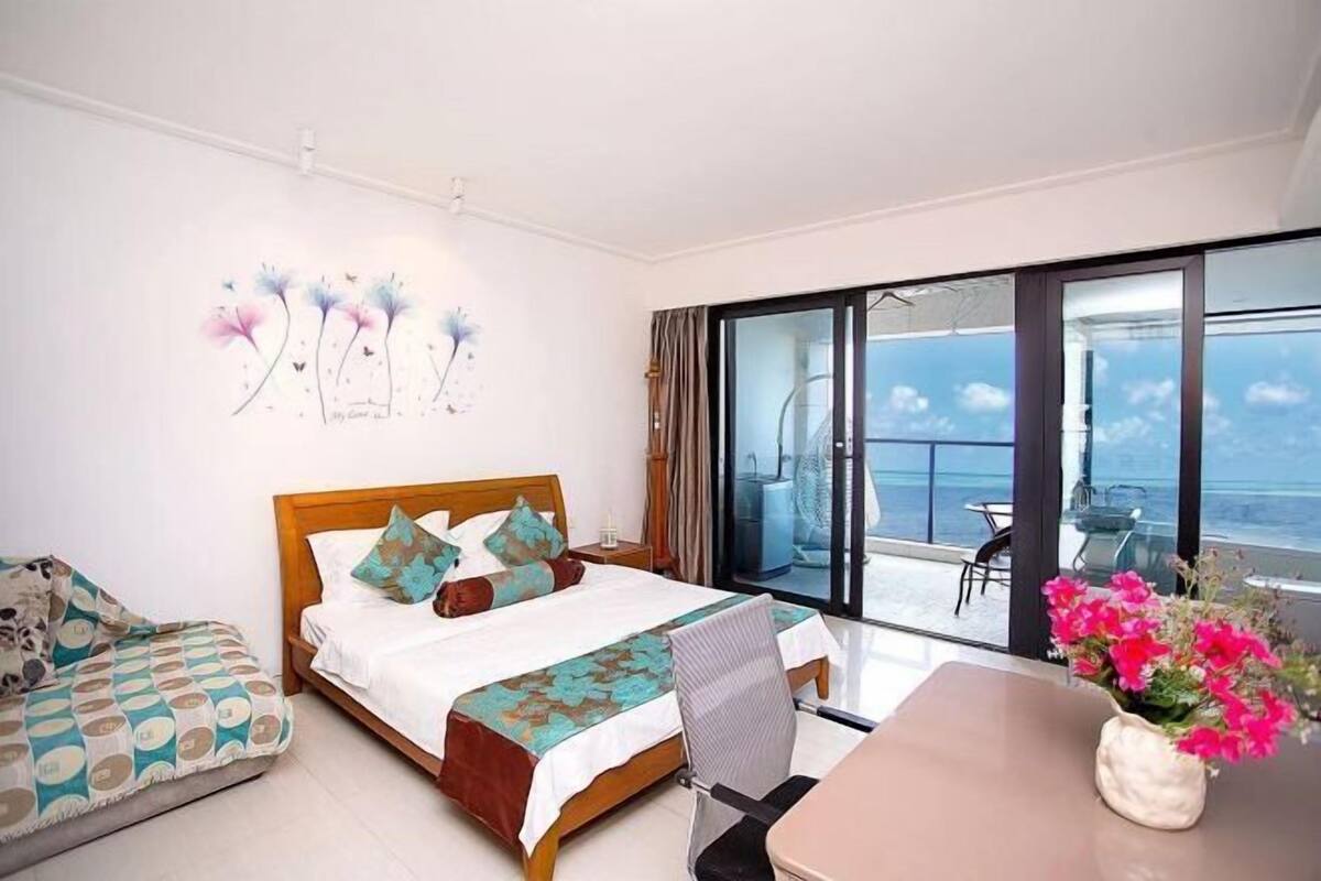 A hotel room with a bed, a desk, a chair, a balcony with a table and chairs, and a view of the sea.