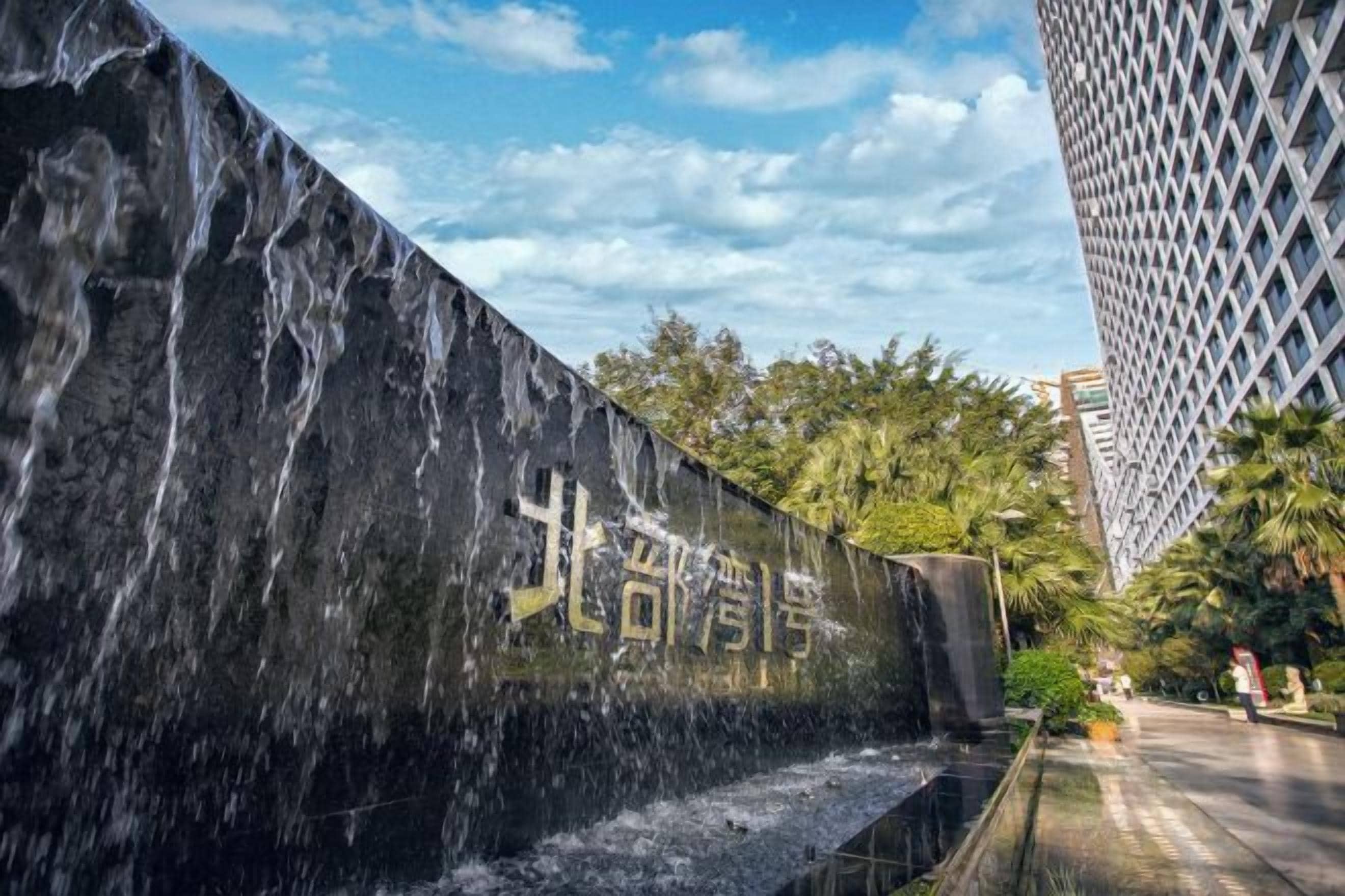 A water feature with a wall inscription, a pathway, and tall buildings in the background.