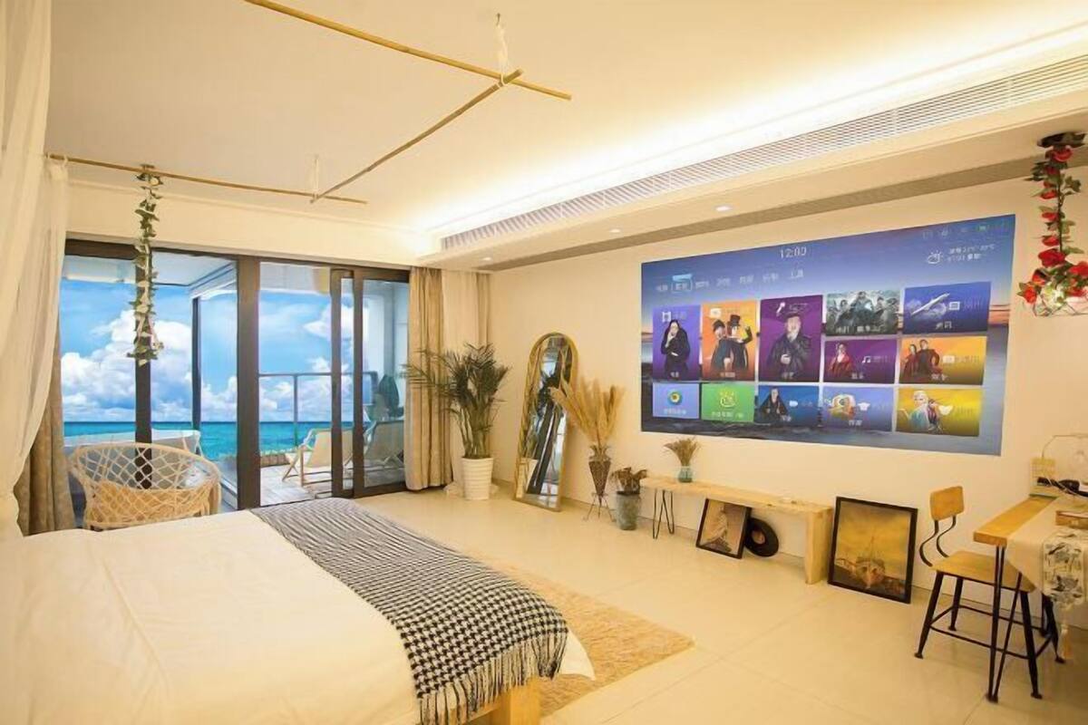 A modern hotel room with a large bed, a balcony with a view, a wall-mounted TV, and a dining area.