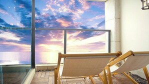 A hammock chair by a large window with a view of a sunset over water.