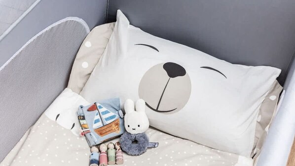 A baby crib with a beige and white polka dot bedding, a large pillow with a bear face, and a small stuffed bunny toy.