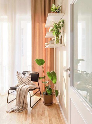 Una habitación con suelo de madera, una silla negra con cojín estampado, una planta grande en maceta y una puerta blanca con panel de vidrio.