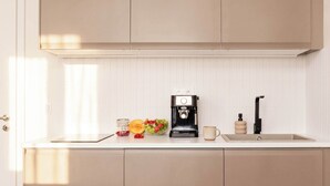 Et køkken med kaffemaskine, vask og skål med frugt.