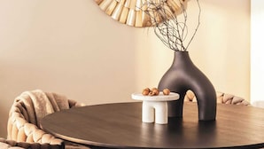 Et rundt spisebord med en mørk overflade, en vase med grene og en tallerken med nødder.