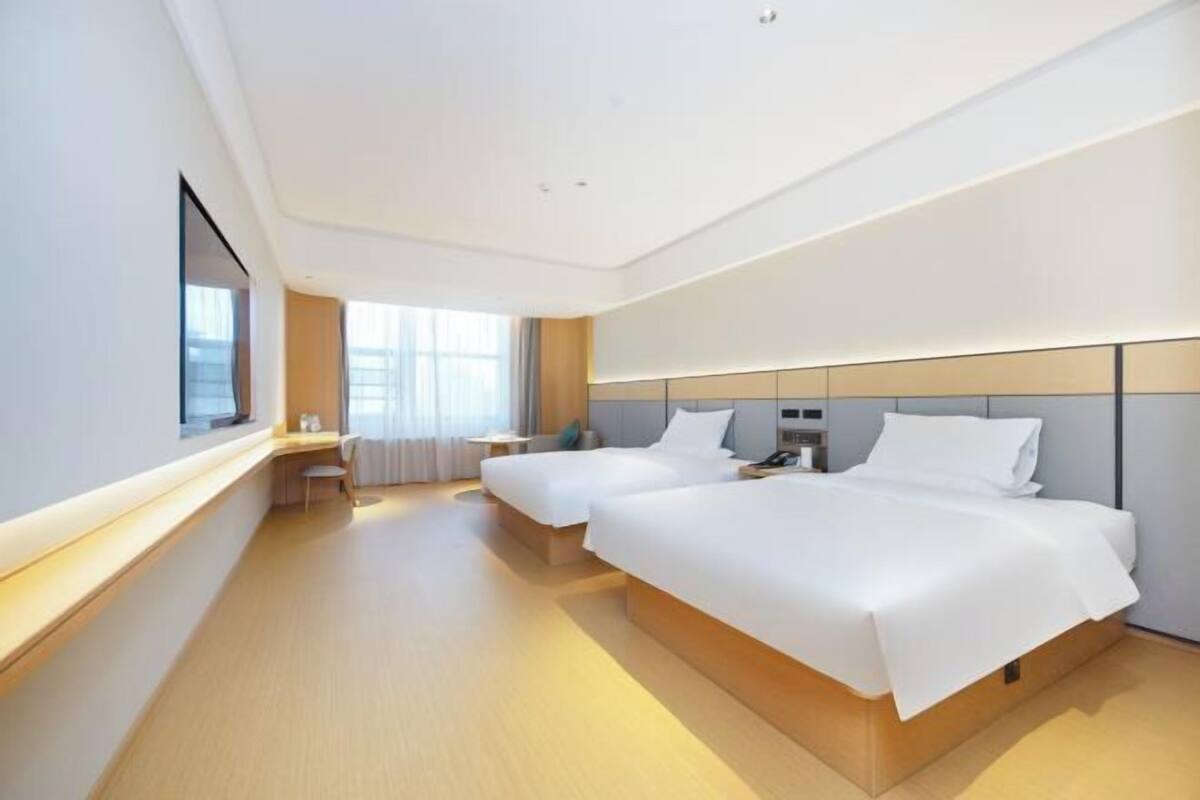 A modern hotel room with two beds, a bedside table, a chair, and a large window.