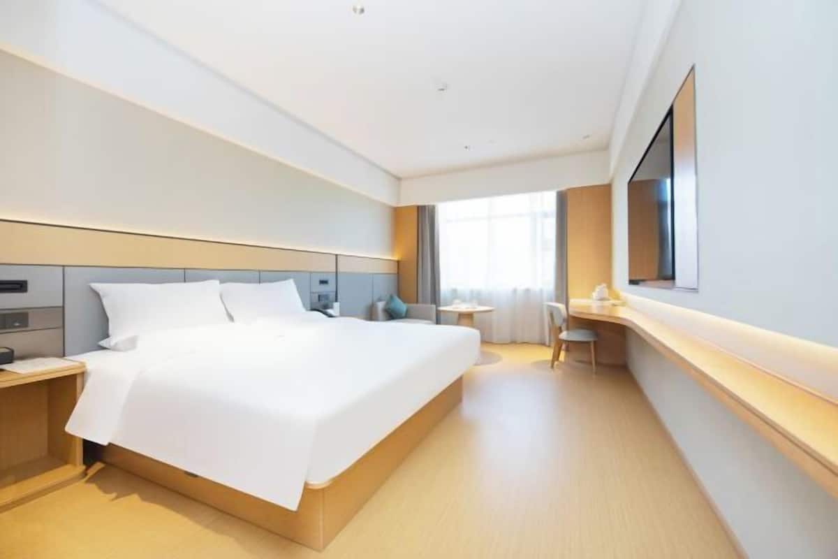 A modern hotel room with a large bed, bedside tables, a desk, and a large window.